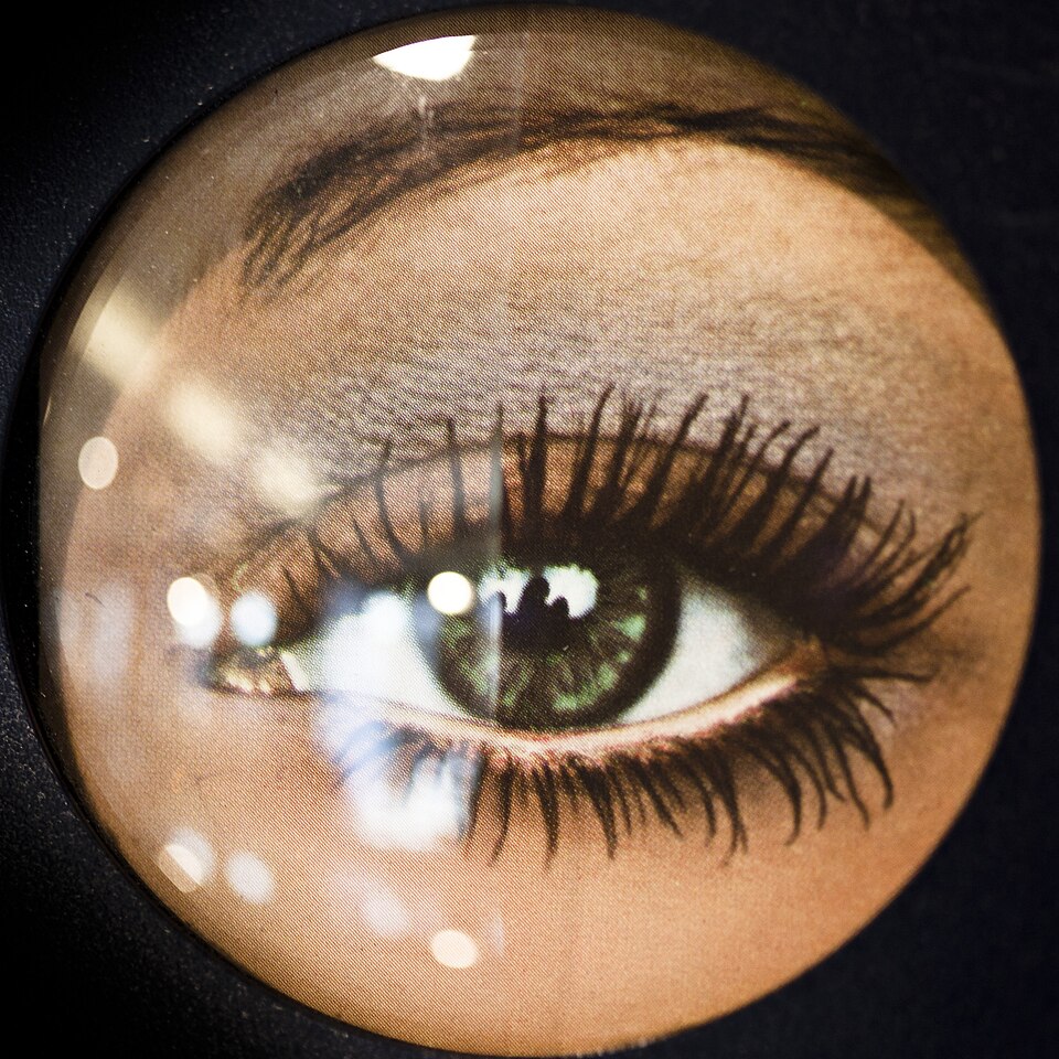 Comparison of an ordinary lens and an antireflection-coated lens over the same image, with strong lamp reflections on the ordinary side and weak reflections on the coated side